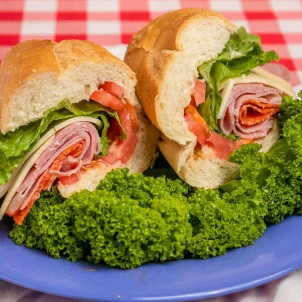 Two halves of a deli sandwich with meat, cheese, lettuce, and tomato on a blue plate.