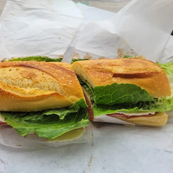 A baguette sandwich, cut in half, filled with green lettuce, cheese, and deli meat.