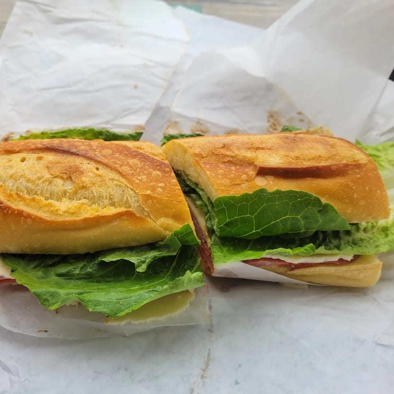 A baguette sandwich, cut in half, filled with green lettuce, cheese, and deli meat.