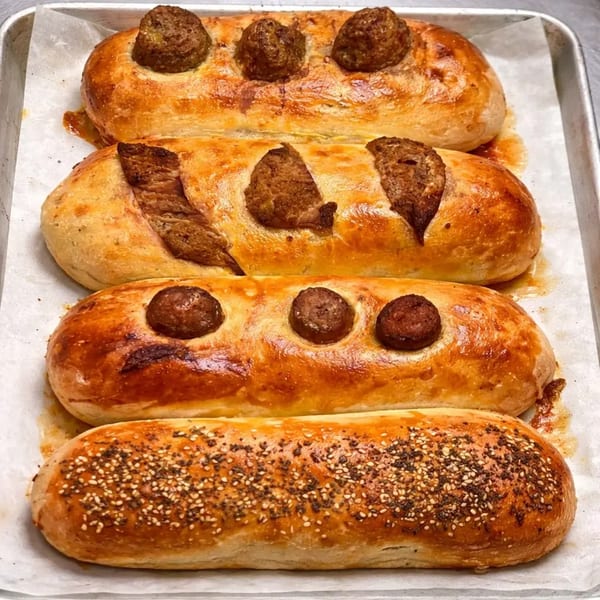 Four golden-brown baked bread loaves, two with meatballs, one with sausage, and one with sesame seeds.