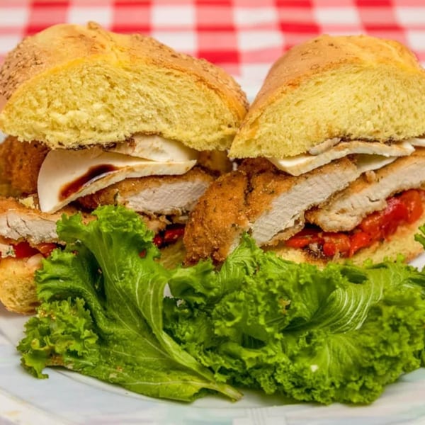 Two chicken parmesan sandwiches with red peppers and cheese, served with fresh green lettuce.