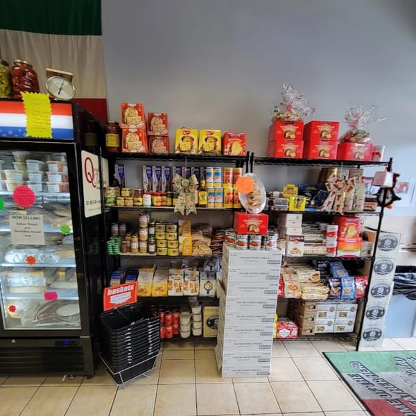 A deli interior with shelves stocked with Italian goods, a refrigerator, and shopping baskets.
