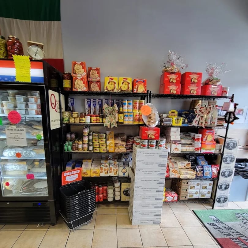 A deli interior with shelves stocked with Italian goods, a refrigerator, and shopping baskets.
