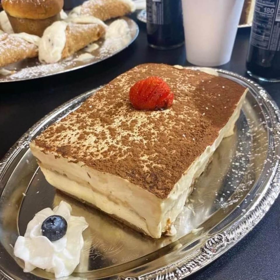 Tiramisu with a strawberry on top, whipped cream, and a blueberry on a silver platter.