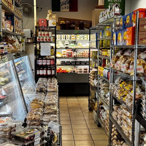 A narrow aisle in a grocery store, with shelves packed with various food items and a refrigerated display case.