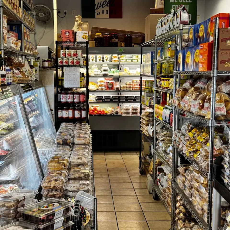 A narrow aisle in a grocery store, with shelves packed with various food items and a refrigerated display case.