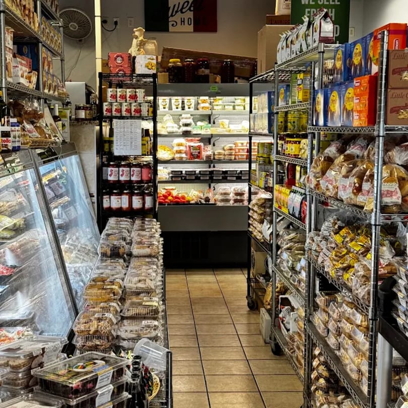 A narrow aisle in a grocery store, with shelves packed with various food items and a refrigerated display case.