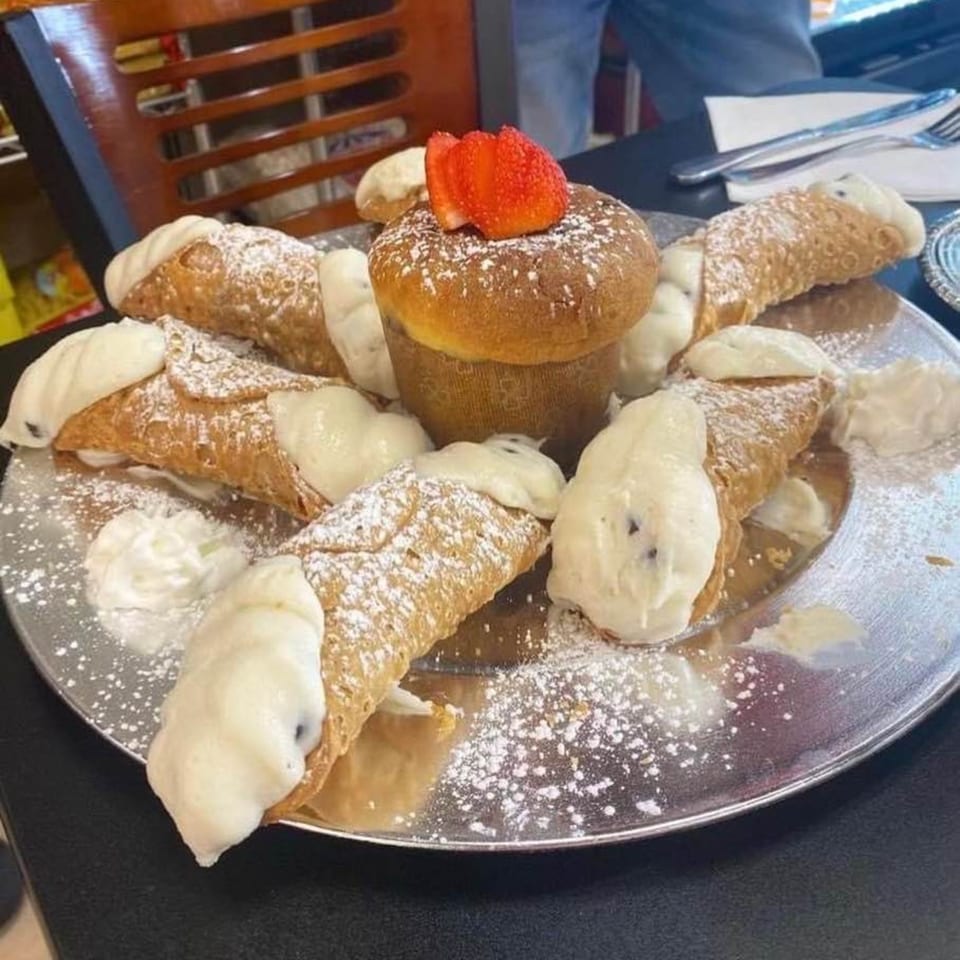 A silver platter with cannolis, a muffin topped with strawberries, and powdered sugar.