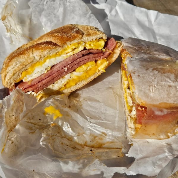A breakfast sandwich with egg and meat, cut in half, on white paper.