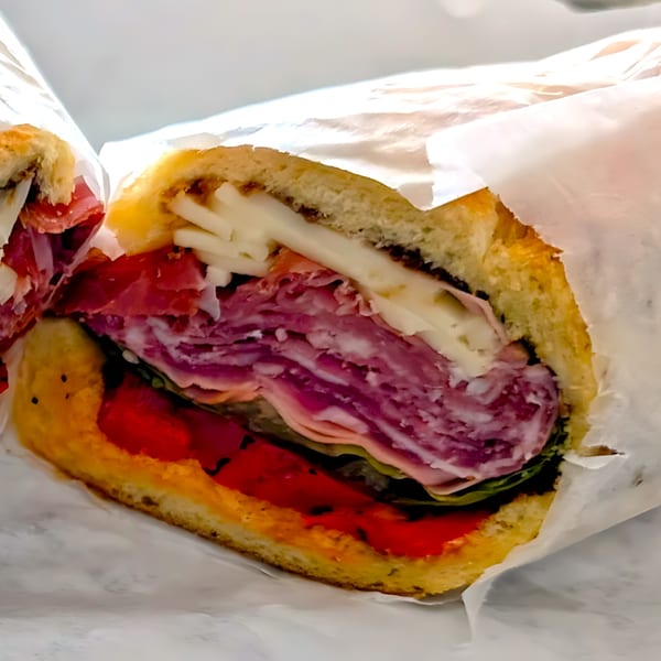 Close-up of a deli sandwich with layers of meat, cheese, and roasted red peppers.