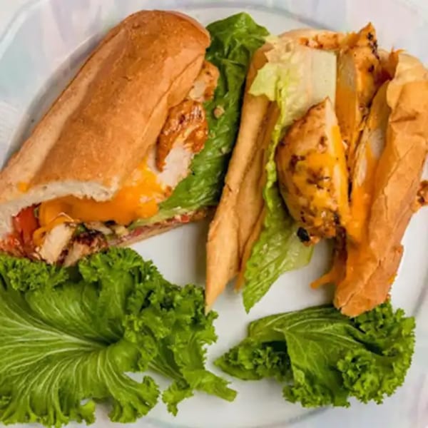 Two chicken and cheese subs with lettuce on a white plate.