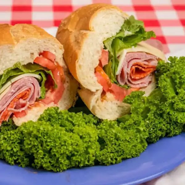 Two halves of a deli sub sandwich with meat, cheese, lettuce, and tomatoes on a blue plate.
